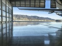 an airplane inside an hanger door in a hangar near a mountain range view and the water