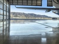 an airplane inside an hanger door in a hangar near a mountain range view and the water