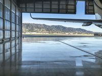 an airplane inside an hanger door in a hangar near a mountain range view and the water