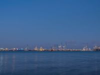 the moon is in the dark sky over the cityscape and water by the shore