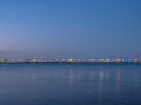 the moon is in the dark sky over the cityscape and water by the shore