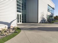 a large building with a driveway next to it and a building outside with grass, plants and trees