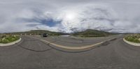 a car driving down a road near mountains under cloudy skies / clouds / looking at the camera