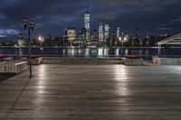 a view of new york city skyline at night from pier on the hudson river side
