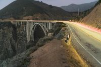 a highway with a bridge spanning a valley with high cliffs and mountains behind it and the light on the road is red