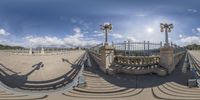 an iron fence with three street lamps in the middle and people walking across it and one looking over the railing