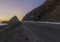 an empty road leads along the side of the mountain towards the ocean and to the rocky mountains