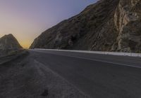 an empty road leads along the side of the mountain towards the ocean and to the rocky mountains