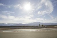 the asphalt surface of an airport runway with mountains in the background and sun rays in the air