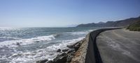 the road beside the ocean is next to the shore line and water is calm and wavy