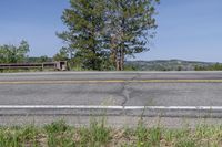 a bench sits in the middle of an empty highway with no traffic and is near a green bush