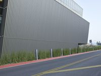 a red traffic light on the corner of the street near a building and some tall grass