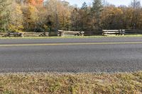 a country highway with trees, fence, and field in the background and grass on both side