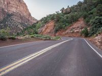 a person on a motorcycle riding along the road between some steep cliffs and trees in the background