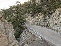 a motorcycle parked on the side of a mountain road near rocks and trees and rock cliffs