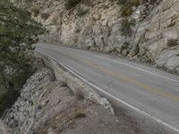 a motorcycle parked on the side of a mountain road near rocks and trees and rock cliffs