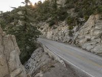 a motorcycle parked on the side of a mountain road near rocks and trees and rock cliffs