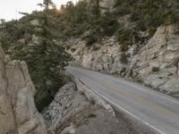 a motorcycle parked on the side of a mountain road near rocks and trees and rock cliffs