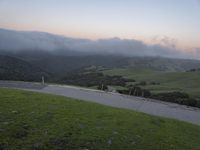 a road on a hill with a green hillside in the background and a mountain behind