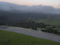 a road on a hill with a green hillside in the background and a mountain behind