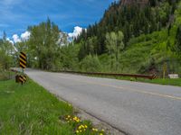 a street leads to a narrow forest with mountains in the background with clouds overhead on an empty mountain road