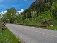 a street leads to a narrow forest with mountains in the background with clouds overhead on an empty mountain road