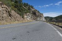 the road is winding down between two cliffs of a mountain range with trees in the background