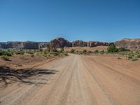 a dirt road in the middle of an open area in the desert, with rocks and bushes on either side