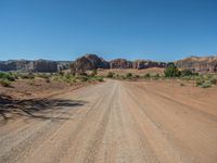 a dirt road in the middle of an open area in the desert, with rocks and bushes on either side