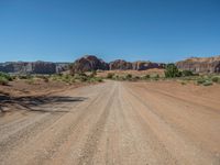 a dirt road in the middle of an open area in the desert, with rocks and bushes on either side