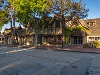 an old house in the middle of a street next to trees and buildings with potted plants