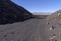 the dirt road goes around some rocks and gravel in an arid area near a mountain