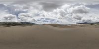 a person standing in the middle of sand dunes under a cloudy sky and clouds in the distance