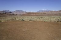 a brown sand field filled with green plants and mountains in the distance are snow capped peaks