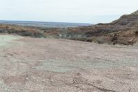 a dirt road leading to a valley of hills and barren ground with a truck driving through it