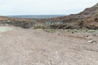 a dirt road leading to a valley of hills and barren ground with a truck driving through it