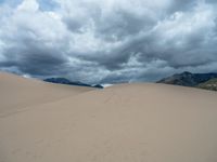 a man walks through a huge sandy field under cloudy skies in the mountains in a remote location