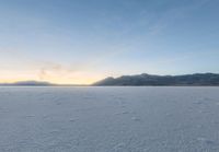 a lone person on a snow covered field of snow in the evening sun setting behind the hills