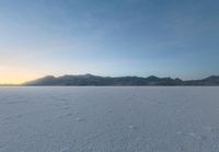 a lone person on a snow covered field of snow in the evening sun setting behind the hills