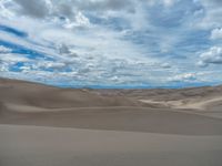 a cloudy day at the desert with clouds overhead and lots of sand dunes in the foreground