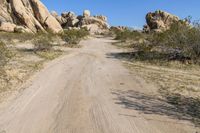 a dirt road that goes through the desert area next to rocks, grass and some plants