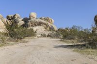 a dirt road that goes through the desert area next to rocks, grass and some plants