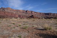 an arid area with dry grass, bushes, and a mountain in the background with a sky