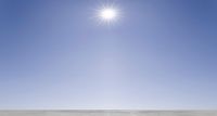 a small motorcycle driving through the desert under a bright sunburstet in the sky