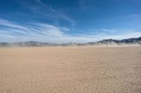 a dirt plain with mountains in the background as seen from a vehicle window in the desert