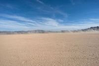 a dirt plain with mountains in the background as seen from a vehicle window in the desert