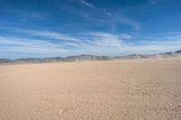 a dirt plain with mountains in the background as seen from a vehicle window in the desert