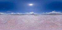 a large desert plain with mountains and snow in the distance near an island surrounded by clouds and a bright sun