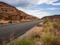 the side of an empty road is surrounded by vegetation and a rocky cliff behind it