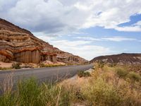 the side of an empty road is surrounded by vegetation and a rocky cliff behind it